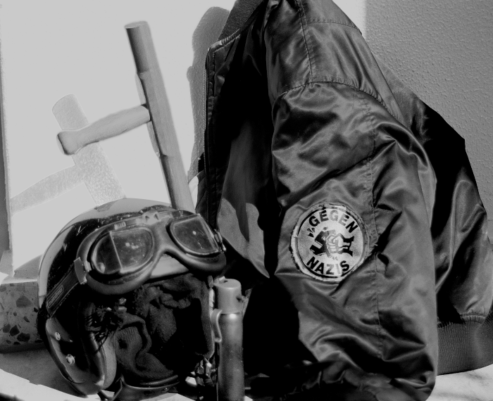 Schwarzweissbild: Jacke mit "GEGEN NAZIS" Patch, Helm und ein Stock, Foto © Christian Ditsch